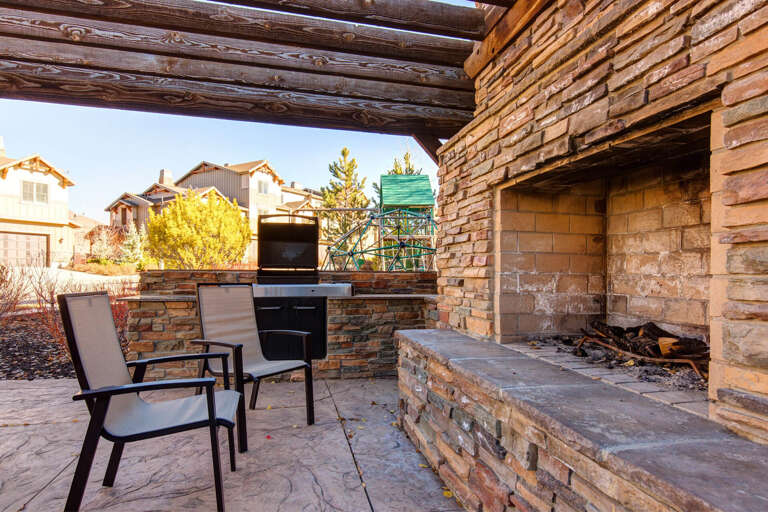 A stunning stone patio with built-in outdoor fireplace and BBQ area, framed by rustic log beams—perfect for cozy evenings under the stars.