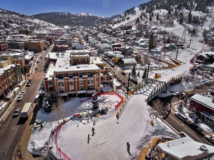 Aerial view of a charming mountain town nestled in a snow-covered valley, featuring ski slopes, lodges, and local shops surrounded by forested peaks.