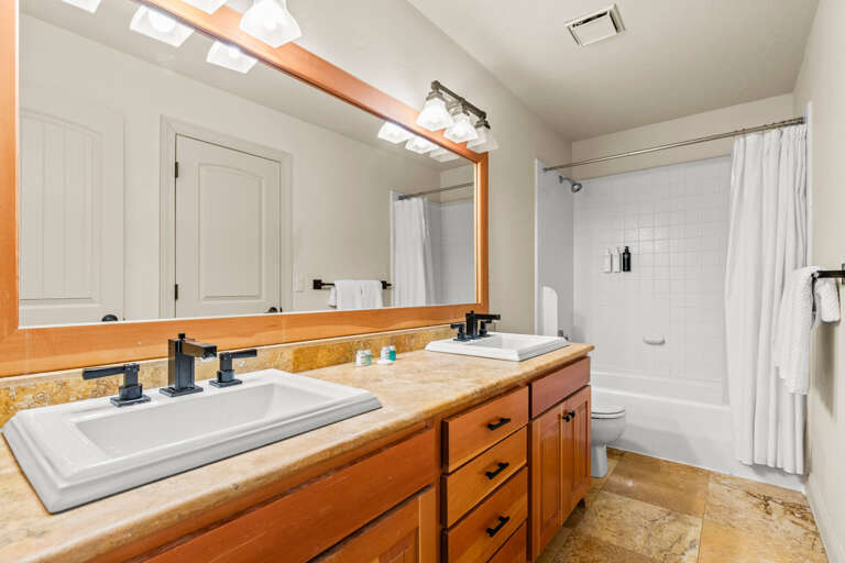 Bright, modern bathroom with natural light from skylights. Your freshly stocked towels await alongside a tub-shower combo and a spacious vanity with warm wooden accents.