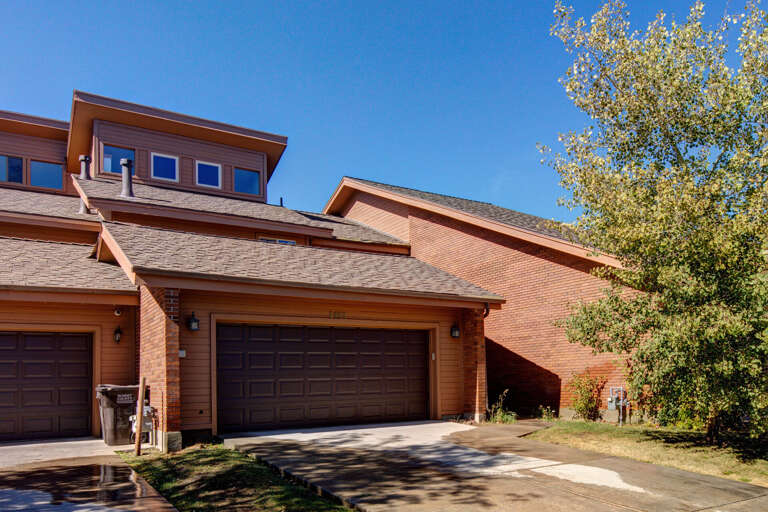 Two-story brick and wood-accented property exterior with private garage and concrete driveway, surrounded by mature trees under clear blue sky.
