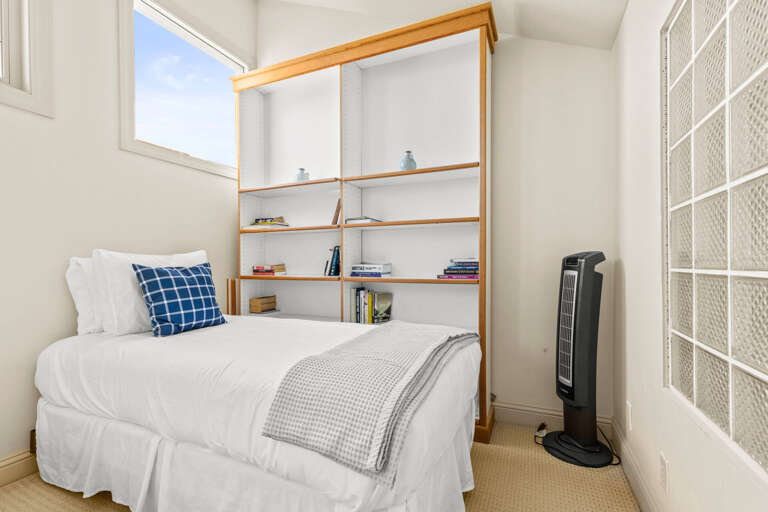 Step into your bright, serene bedroom where crisp white linens and a plush pillow invite restful sleep. Natural light pours in, while open shelving adds character and charm.
