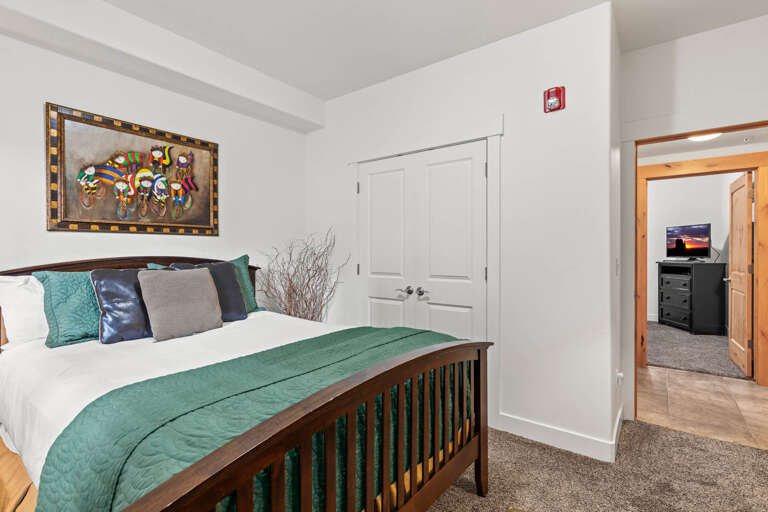 Step into your restful retreat with a plush queen bed dressed in crisp linens and elegant teal accents. Wake to vibrant artwork and natural light, with another cozy room just beyond.