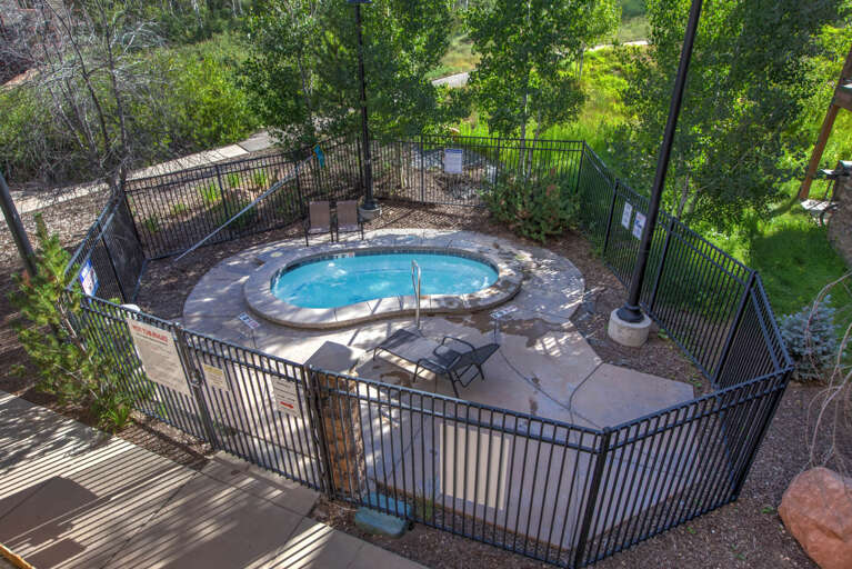 Aerial view of an outdoor hot tub area surrounded by trees and natural landscaping, with seating and a private fenced enclosure for relaxation.