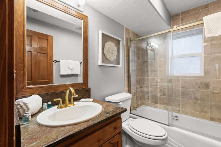 A thoughtfully designed bathroom featuring warm wood tones and elegant stone tilework. Fresh towels and modern fixtures await your arrival, with a spacious tub-shower combination perfect for unwinding after your day.