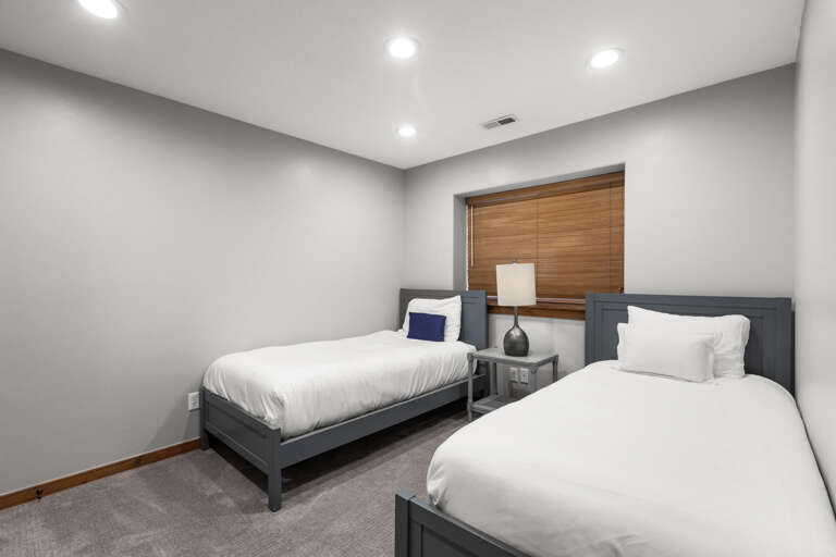 Your peaceful twin bedroom awaits, featuring two cozy beds with crisp linens, soft carpeting underfoot, and warm bamboo blinds filtering natural light for restful mornings.