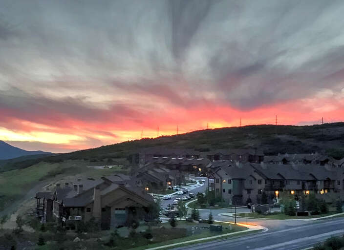 Dramatic sunset paints the sky in vibrant hues over this hillside residential community, creating a stunning backdrop for the property's location.