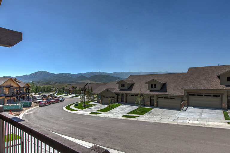 A residential neighborhood with newly developed homes set against a backdrop of dramatic mountain ranges and expansive blue skies.