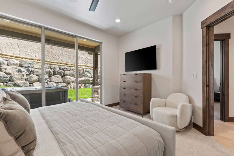 Unwind in your serene bedroom with views of the outdoor patio through expansive glass doors, plush furnishings, and modern entertainment at your fingertips.