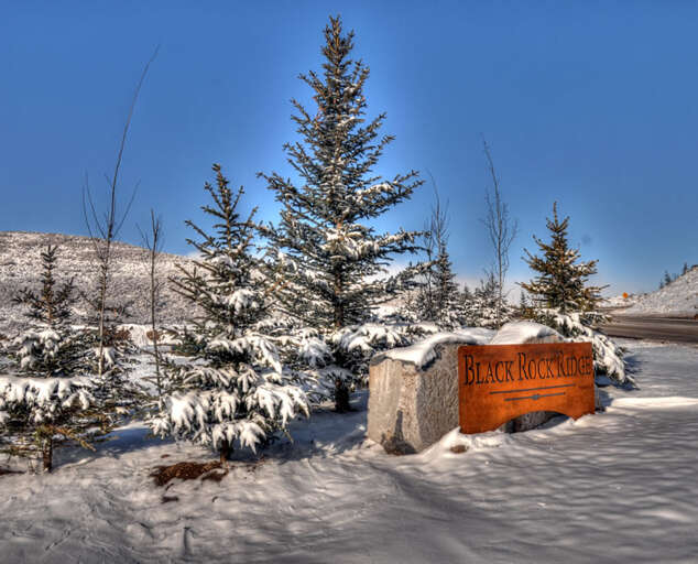Black Rock Ridge entrance marker surrounded by snow-dusted pines and mountain views, marking the property location in a serene winter landscape.