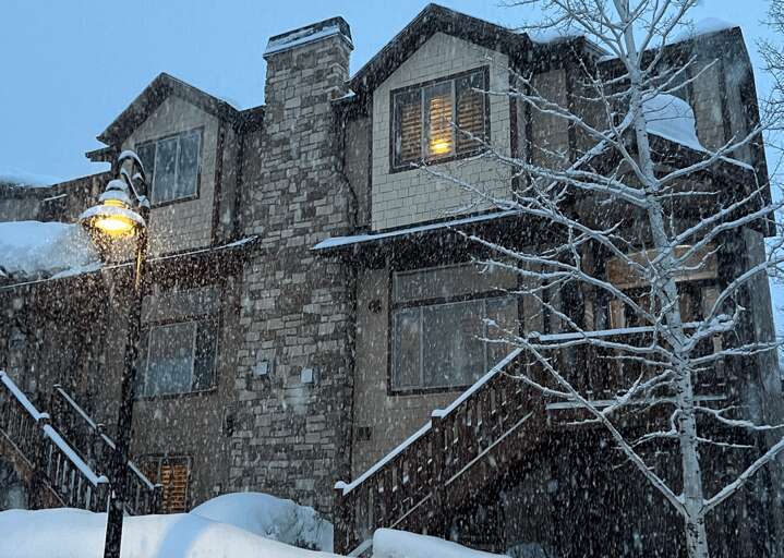 Snowy evening at this charming brick retreat, where warm light glows from the windows and fresh powder blankets the property in peaceful winter magic.