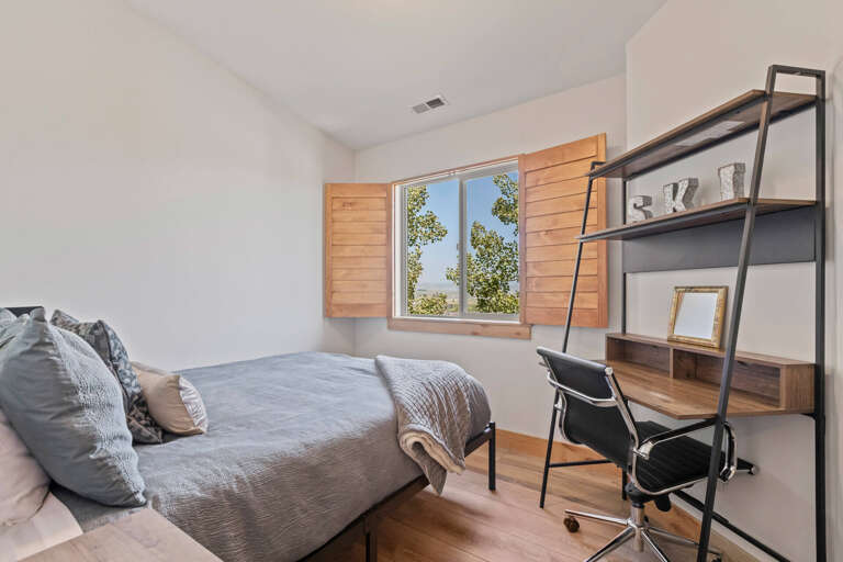 Your peaceful bedroom features a comfortable bed and workspace, with charming wooden shutters framing a scenic view of the surrounding greenery and countryside.