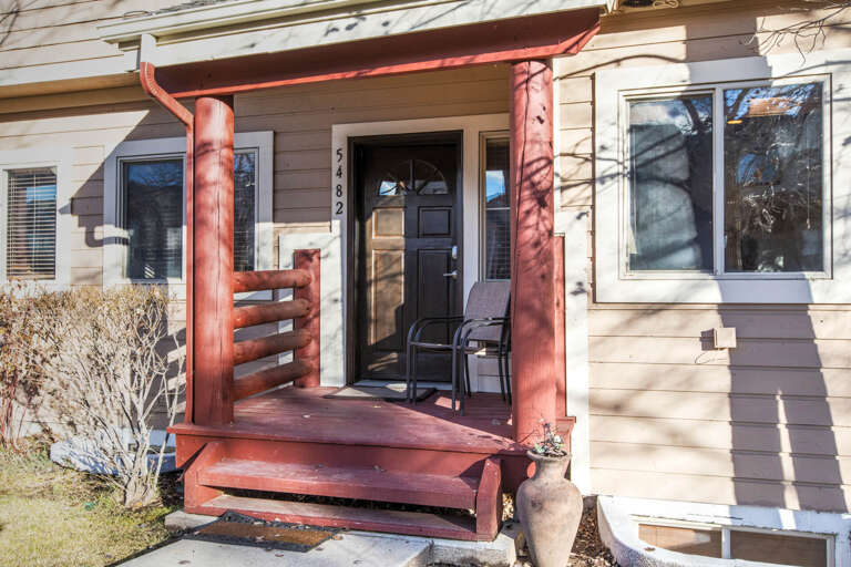 A warm, rustic entrance welcomes you at unit 5462 with its charming red-stained wood porch and inviting front door—a cozy mountain retreat awaits beyond the threshold.