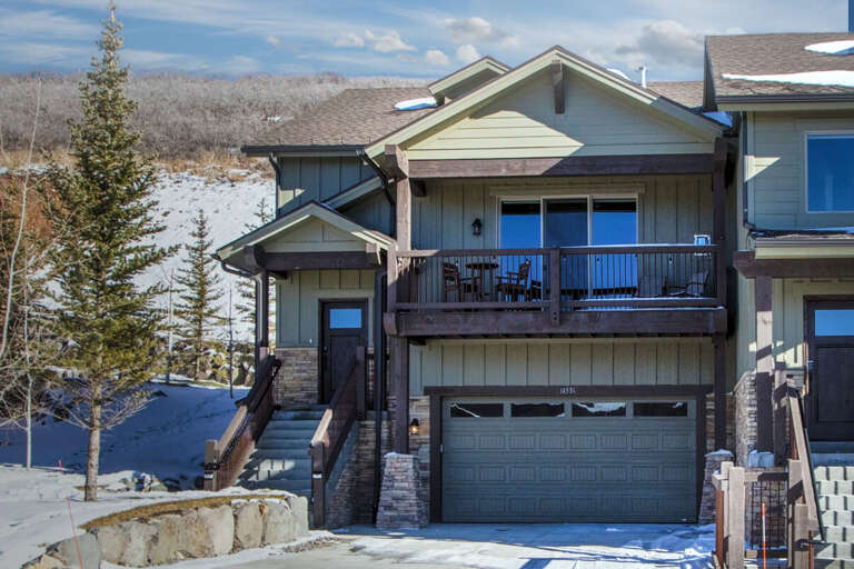 Modern mountain townhome featuring a private balcony, garage access, and winter scenery with snowy slopes visible in the background—a quiet retreat close to outdoor adventure.
