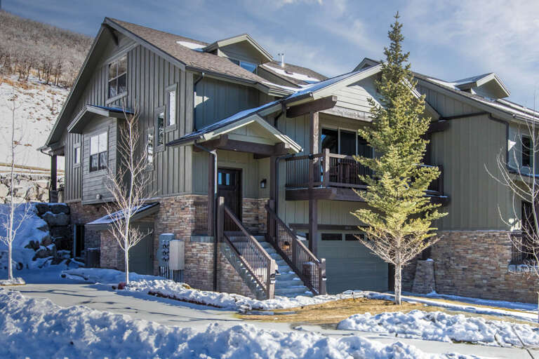 A modern mountain retreat nestled against snowy slopes, featuring stone and wood accents, multiple balconies, and ski-in access—perfect for a winter getaway surrounded by alpine beauty.