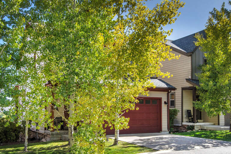 A charming property nestled among mature trees with golden autumn foliage, featuring a welcoming entrance and driveway surrounded by natural beauty.
