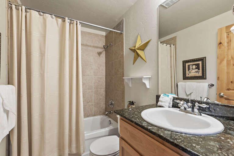 Your private bathroom features warm wood cabinetry, a sleek dark countertop, and a relaxing tub-shower combo—everything you need to unwind after a day of adventure.