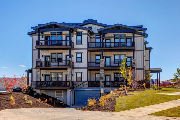 Modern multi-level building featuring contemporary architecture with stone accents, spacious balconies, and seasonal landscaping in a peaceful residential setting.