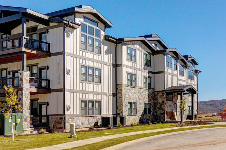 A modern multi-story vacation property blending stone and contemporary siding, framed by rolling hills and clear blue skies in a peaceful setting.