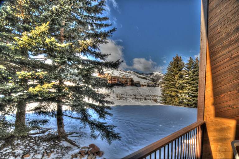 A winter mountain escape framed by evergreens, where fresh snow blankets the landscape and neighboring lodges dot the hillside beyond.