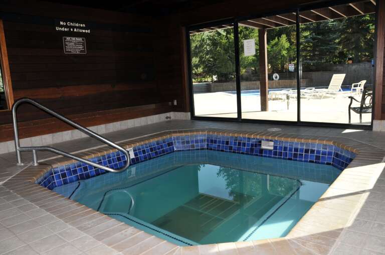 Unwind in your private indoor hot tub with serene views of the outdoor pool through floor-to-ceiling windows. Lush greenery creates a peaceful retreat for ultimate relaxation.