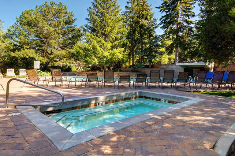 A serene pool area surrounded by towering pines offers abundant sun and shade. Lounge on comfortable chairs, soak in the hot tub, and unwind in this peaceful outdoor retreat.