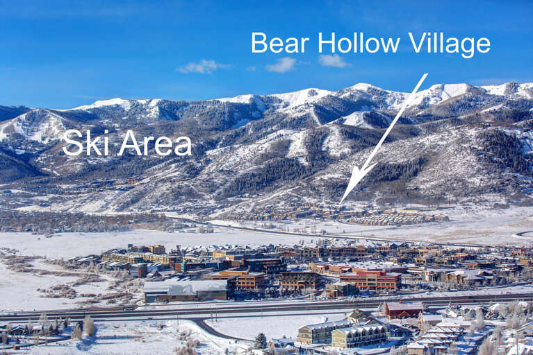 An aerial winter view reveals the ski resort town nestled against snow-capped mountains, with Bear Hollow Village and ski slopes visible in the pristine landscape.