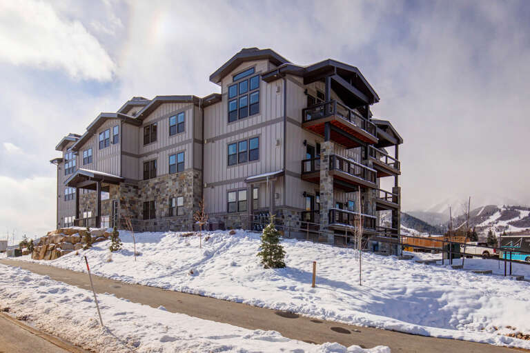 A modern mountain property with stone and wood exterior, featuring multiple balconies and large windows, set against a snowy alpine landscape.
