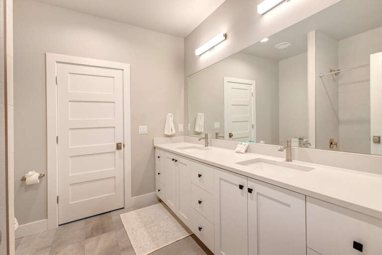 Your private bathroom features dual vanities with bright lighting, elegant white cabinetry, and soft gray walls—perfect for getting ready together or enjoying personal space.