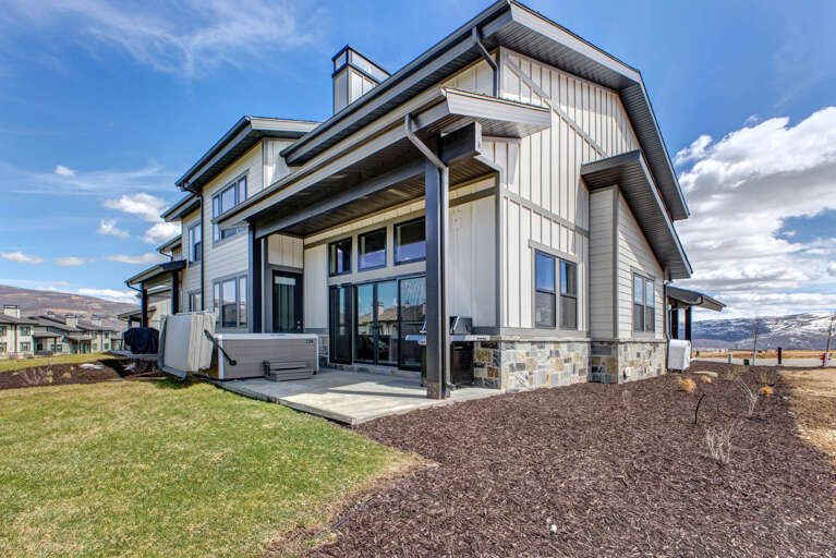 Modern mountain retreat featuring contemporary architecture with stone accents, expansive windows, and a private hot tub set against stunning valley and mountain vistas.