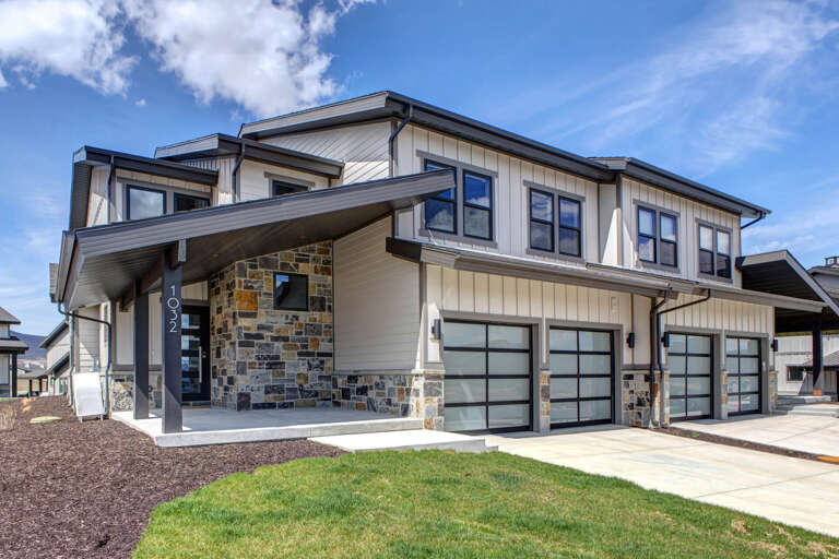 Modern vacation rental property with contemporary architectural design, featuring natural stone accents, sleek metal-framed garage doors, and bright mountain-style finishes in a peaceful residential neighborhood.