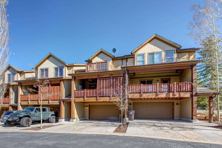 A multi-unit property featuring mountain-style architecture with spacious balconies, private garages, and views of the surrounding natural landscape under clear blue skies.