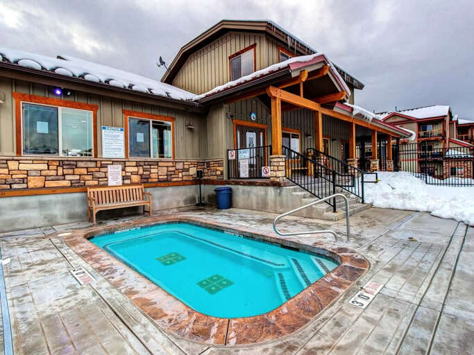 Mountain lodge hot tub surrounded by snow-capped roofs and timber accents, blending alpine charm with a welcoming entrance just steps from the warmth indoors.