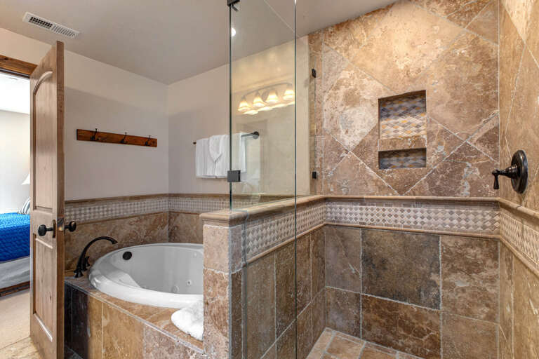 Step into your private spa-like bathroom with a luxurious soaking tub and spacious walk-in shower, where earthy stone tiles create a warm, relaxing retreat after your day's adventures.