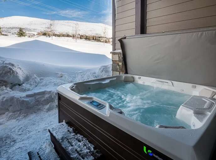 A winter mountain retreat framed by snowy slopes and crisp blue skies. The private hot tub awaits after days on the slopes, offering warmth and relaxation with scenic alpine views.