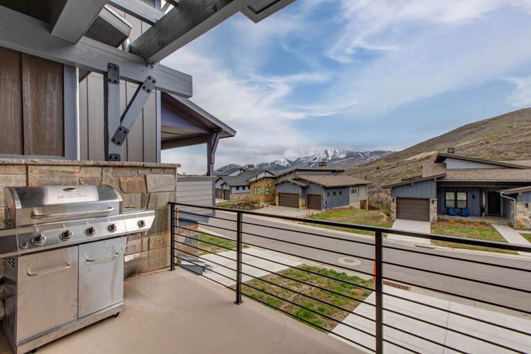 This covered balcony features a gas grill ready for outdoor cooking, with stunning mountain vistas and a peaceful residential setting framing the scene.