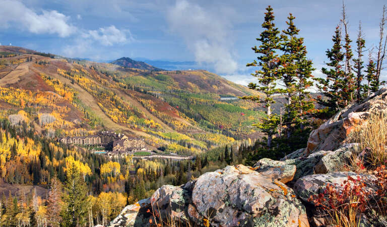 The property sits surrounded by striking mountain terrain with vibrant autumn foliage painting the hillsides in gold and crimson beneath a partly cloudy sky.
