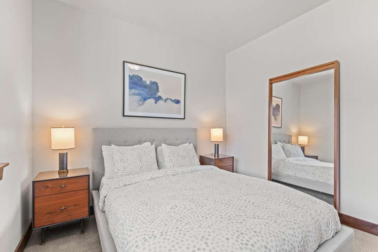 Sink into plush bedding under soft ambient lighting. Your serene retreat features modern nightstands and a calming art piece—perfectly styled for restful sleep.