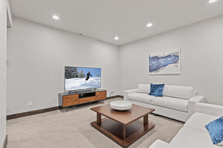 Sink into plush white couches in this bright, minimalist lounge—your perfect spot to unwind after a day on the slopes, with a large TV for movie nights and cozy modern touches.