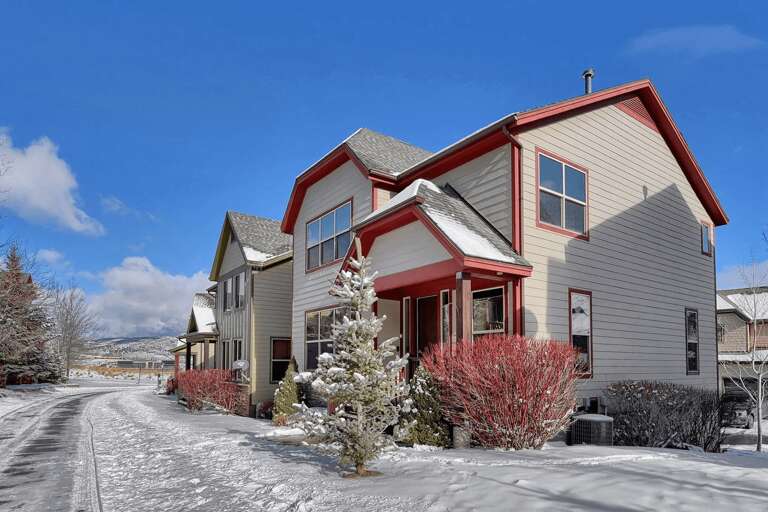Two-story vacation rental with red trim and modern design, located in a quiet mountain neighborhood with snow-dusted landscaping and scenic mountain backdrop.