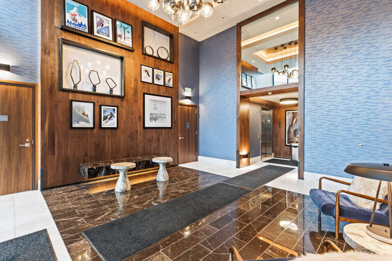 Step into a sophisticated lobby where warm wood tones meet modern elegance, with striking vintage ski art setting the scene for your mountain retreat.
