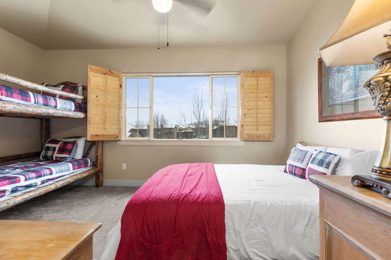 Your spacious bedroom features a comfy queen bed plus bunk beds—perfect for families. Natural light streams through large windows framing peaceful winter views, while rustic wood accents add warmth.