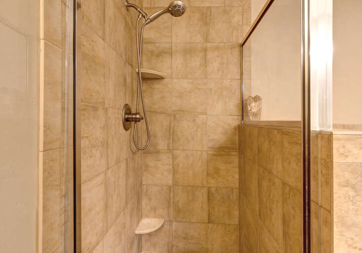 Step into your private walk-in shower featuring elegant travertine tile, a rainfall showerhead, and built-in shelf for your essentials—designed for a refreshing start to your day.