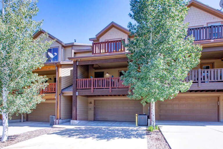 Multi-level townhome-style property featuring balconies and garages, framed by tall aspens under clear blue skies.