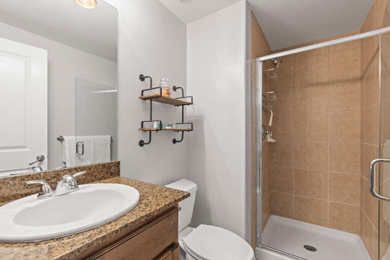 Enjoy a clean, modern bathroom with a sleek walk-in shower, granite countertop, and thoughtful shelving—your perfect spot to refresh after a day of exploring.