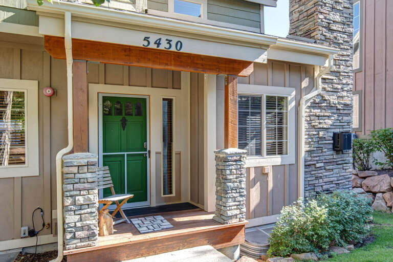 The property entrance at 5430 features a welcoming green door with modern stone and wood accents, surrounded by landscaped greenery and a cheerful covered porch.