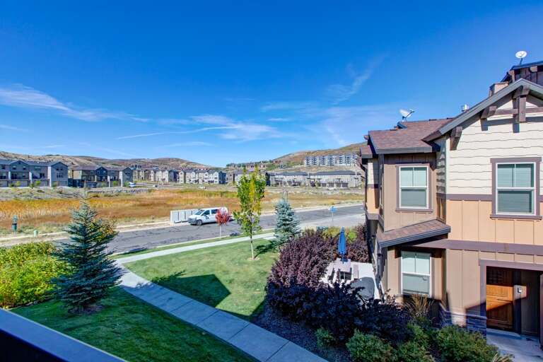 Daytime view capturing the property's setting in a developing residential neighborhood with nearby homes, distant hills, and glimpses of street activity under a clear blue sky.