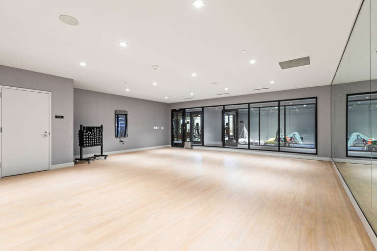 A spacious modern fitness studio with polished wood floors, floor-to-ceiling mirrors, and views into the adjacent gym—your private space for yoga, dance, or group workouts.