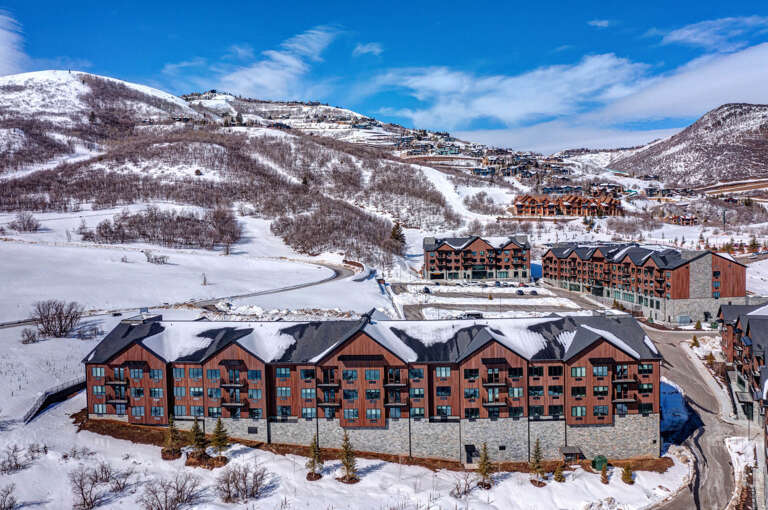An aerial perspective reveals the resort property nestled at the base of snow-covered mountain slopes, with ski runs visible on surrounding hillsides during the winter season.
