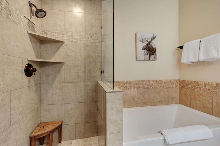 Your private bathroom offers a spacious walk-in shower with built-in niche storage and a relaxing soaking tub, elegantly tiled in warm neutral tones for a spa-like retreat.