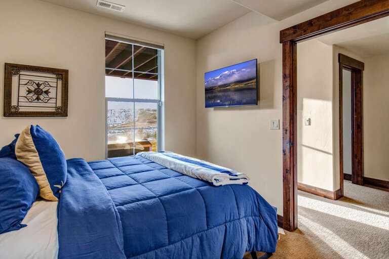 Sink into crisp linens and wake to peaceful winter views. Your cozy bedroom features a mounted TV, rustic wood accents, and serene natural light streaming through the window.